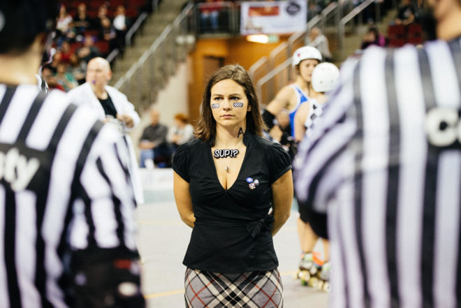 Image of Anayalator wearing a necklace that says "SUP!?" facing a referee crew 